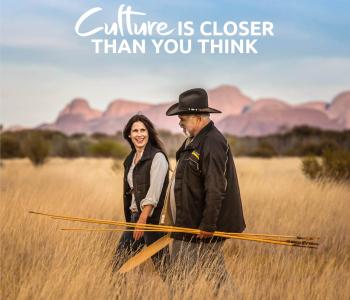 image of woman with Aboriginal guide holding spearks and walking through long grass