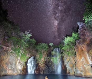 night image of women in waterfalls with stars above