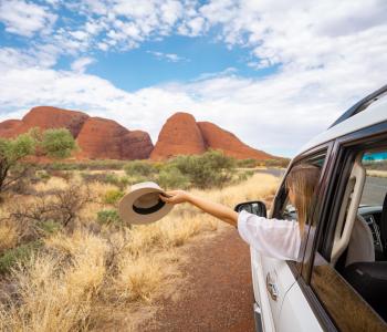 image of woman holding hat out window as driving towards red boulders