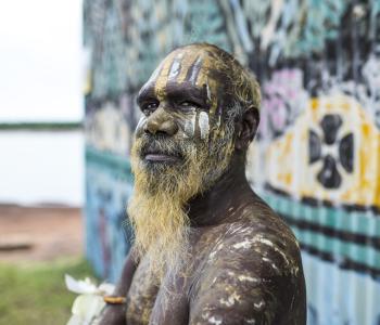 image of Aboriginal man standing in front of buildling painted with art