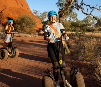 two women riding segways with Uluru in background