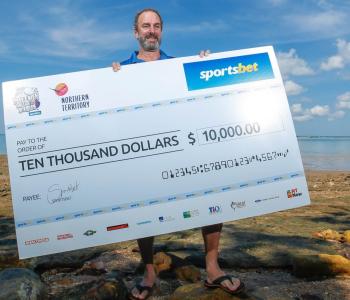 Man holding up $10,000 cheque at beach