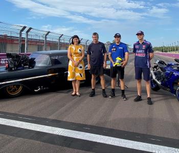 Group of people standing in front of a drag car and Superbike