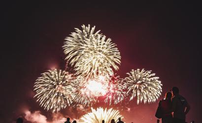 A crowd of silhouetted beachgoers watch a night-time fireworks display during Territory Day