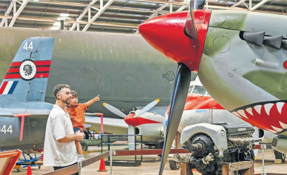 Father Holds his young son as they look up to a World War 2 era fighter jet at the Darwin military museum
