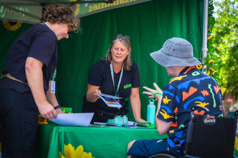 Two women talking with a man in a wheelchair in a tent